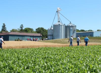 People walking through farm fields with farm buildings